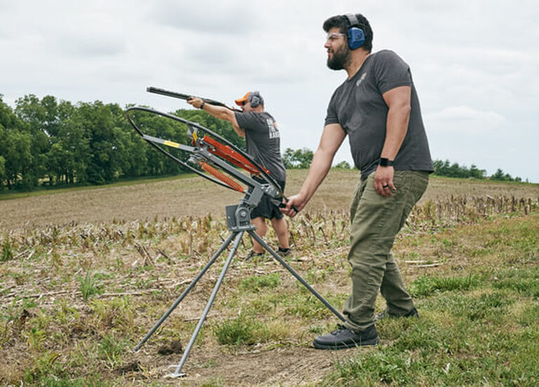 Man wearing ear protection operating SkyBird Manual Trap while target shooter wearing ear protection takes aim with a shotgun